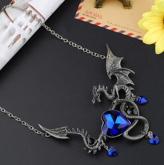 Dragon-shaped necklace with blue heart pendant on a dark surface