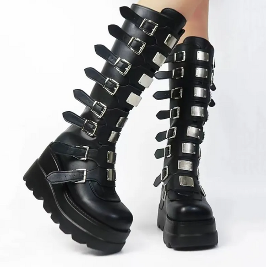 A pair of black knee-high platform boots with multiple silver buckle straps, shown worn on a person's legs against a plain white background.