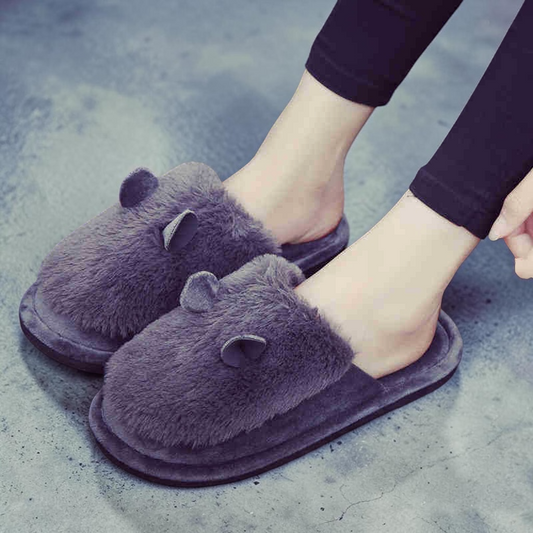 A person wearing plush gray animal-ear slippers with black leggings, standing on a gray concrete floor.