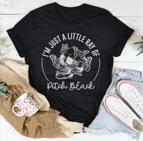 Black t-shirt with a graphic design and text, placed on a wooden surface with casual items around.