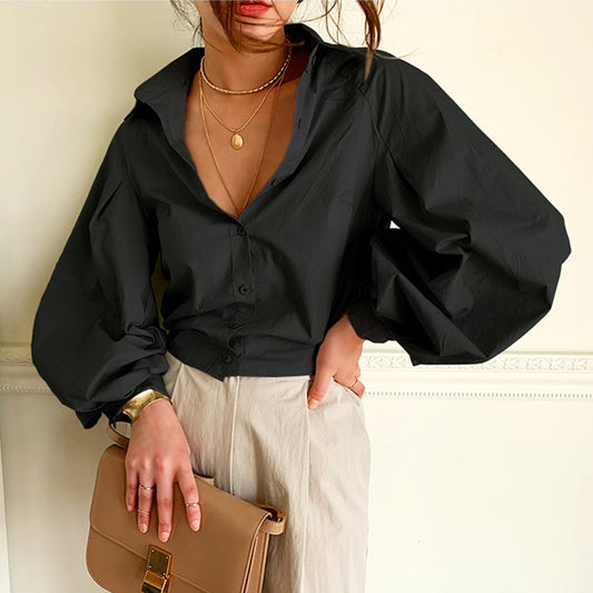 Person wearing a black blouse and holding a beige handbag against a neutral background