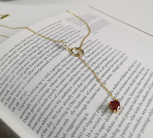 Delicate gold necklace with a red gemstone on an open book