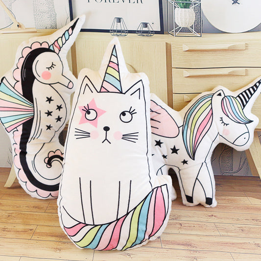 Three plush unicorn-shaped throw pillows in white with pastel rainbow stripes and black line-art details, arranged on a light wood floor in front of a wooden cabinet.