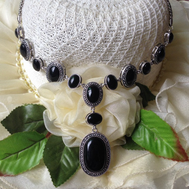 Necklace with black stones and silver accents on a white flower and green leaves background