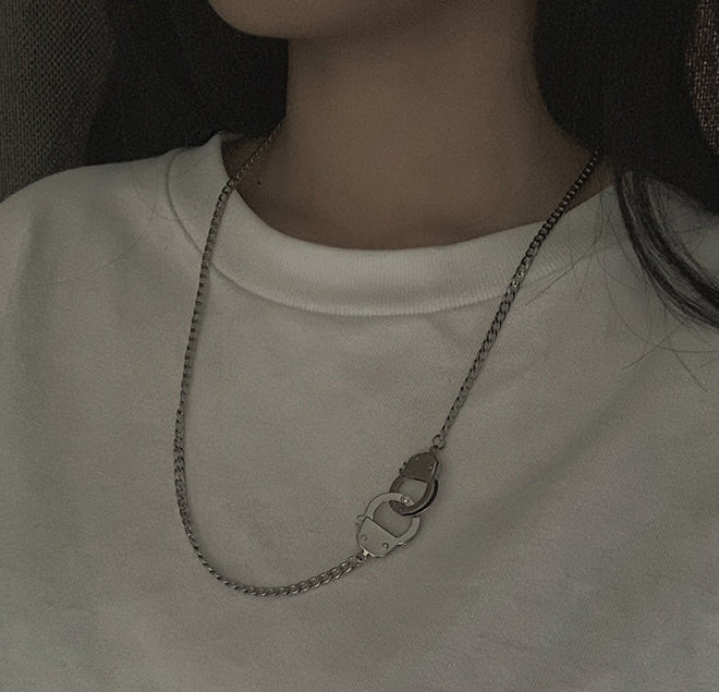 A close-up of a person wearing a silver chain necklace with a double-ring clasp, styled with a white crewneck sweatshirt.