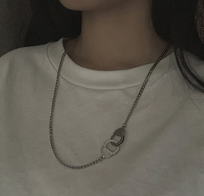 A close-up of a person wearing a silver chain necklace with a double-ring clasp, styled with a white crewneck sweatshirt.