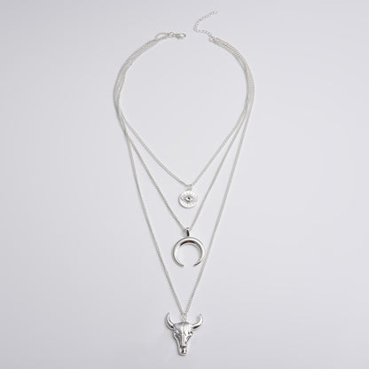Silver layered necklace with bull head and moon pendant on a light gray background