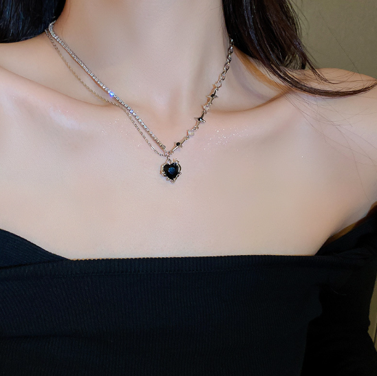 Necklace with a black heart pendant worn by a person against a neutral background