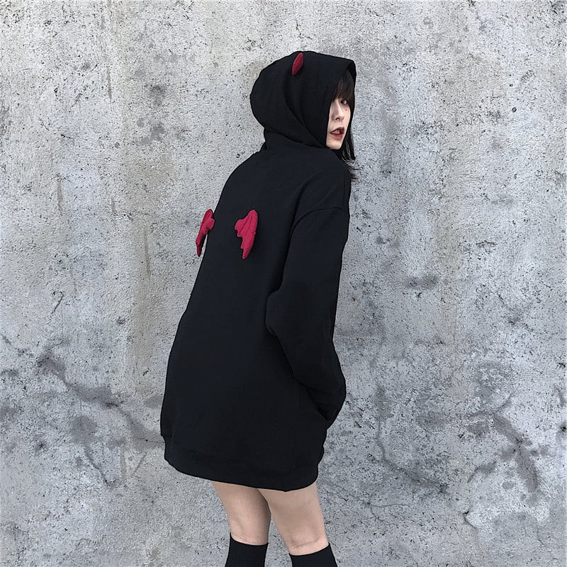 Person wearing a black hoodie with red accents against a gray concrete wall