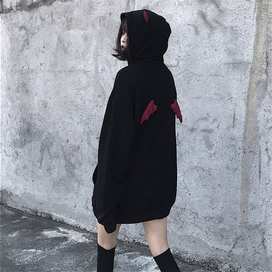Person wearing a black hoodie with red accents against a gray wall.