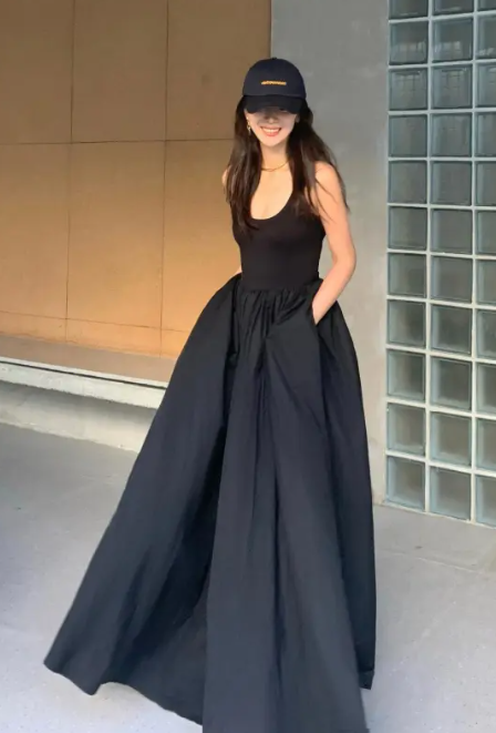 Woman wearing a long black dress and cap outdoors.