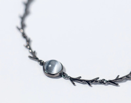 A close-up of a dark metallic branch-style necklace with a smooth oval gray stone pendant, photographed on a clean white background.