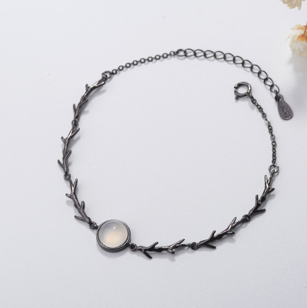 A dark gunmetal branch-link bracelet featuring a central oval cabochon stone with a milky white center and dark rim, displayed on a clean white background.