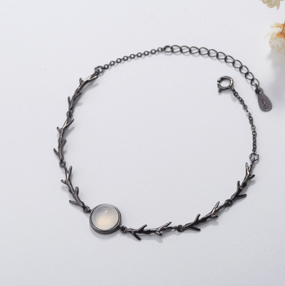 A dark gunmetal branch-link bracelet featuring a central oval cabochon stone with a milky white center and dark rim, displayed on a clean white background.