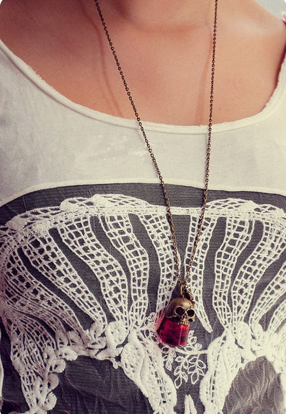 Necklace with a skull and red gemstone pendant on a person wearing a white lace top.