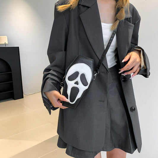 Person wearing a dark gray coat holding a black bag with a white face design.