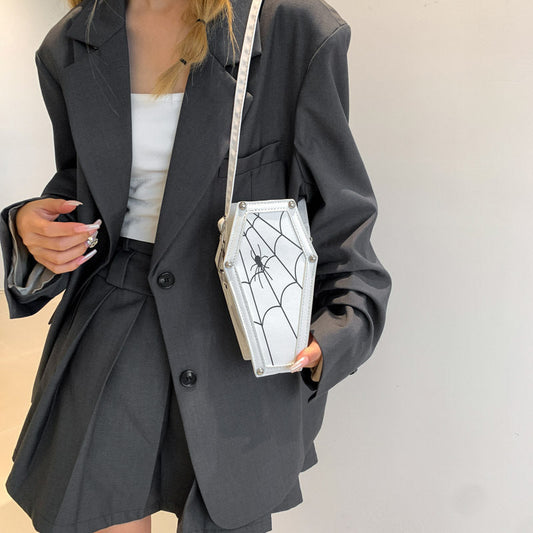 Person wearing a black blazer holding a coffin-shaped handbag with spider web design.