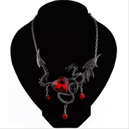 Gothic-style necklace with red heart and dragon design on a black stand.