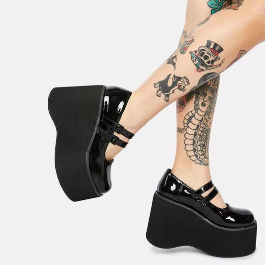 Black platform shoes worn with tattooed legs on a white background