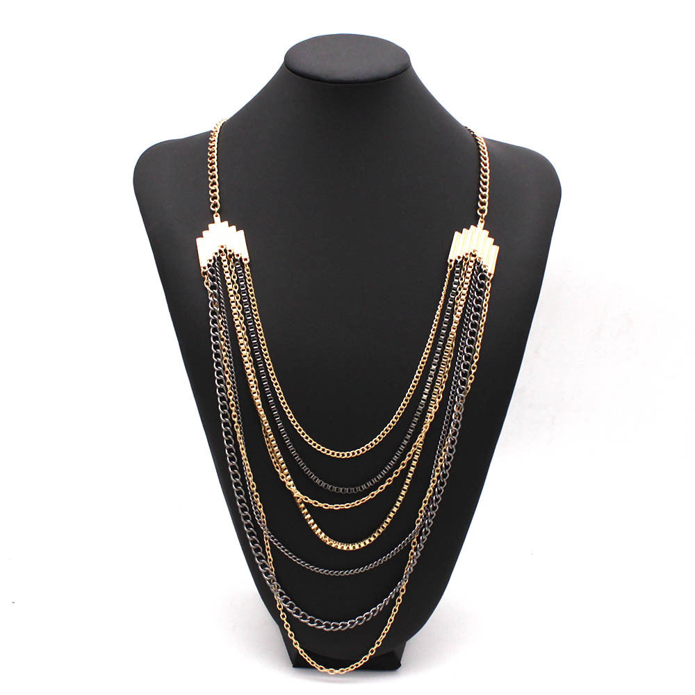 A multi-strand statement necklace displayed on a black mannequin bust against a white background. The necklace features multiple layers of gold and silver-tone chains with geometric gold-tone end pieces.