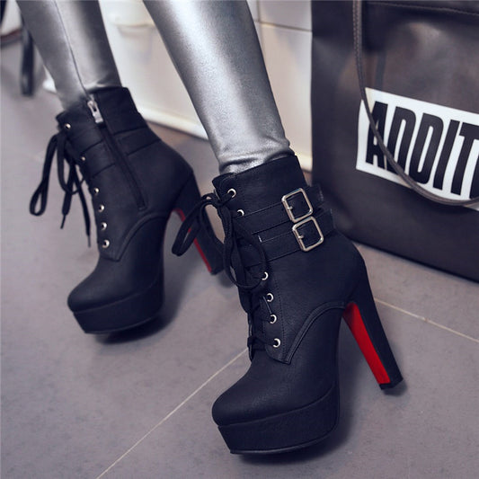 Black platform boots with red soles worn by a person, with a black bag in the background.