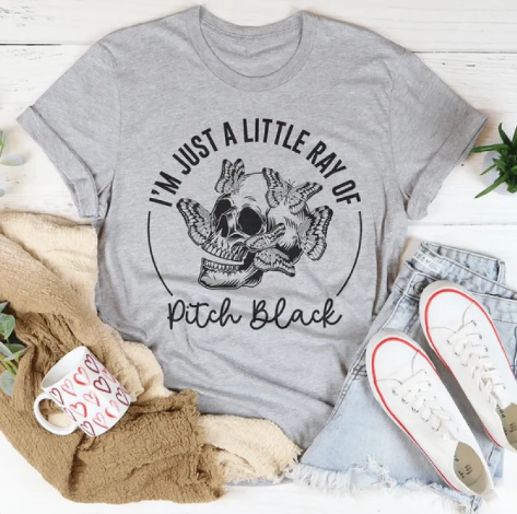 Gray t-shirt with skull graphic and text, placed on a surface with shoes and mug.
