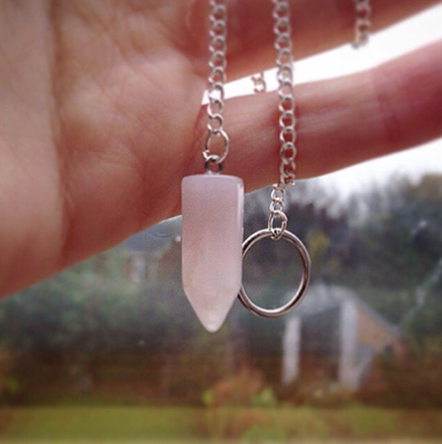 Necklace with a pink crystal pendant and silver ring on a blurred natural background