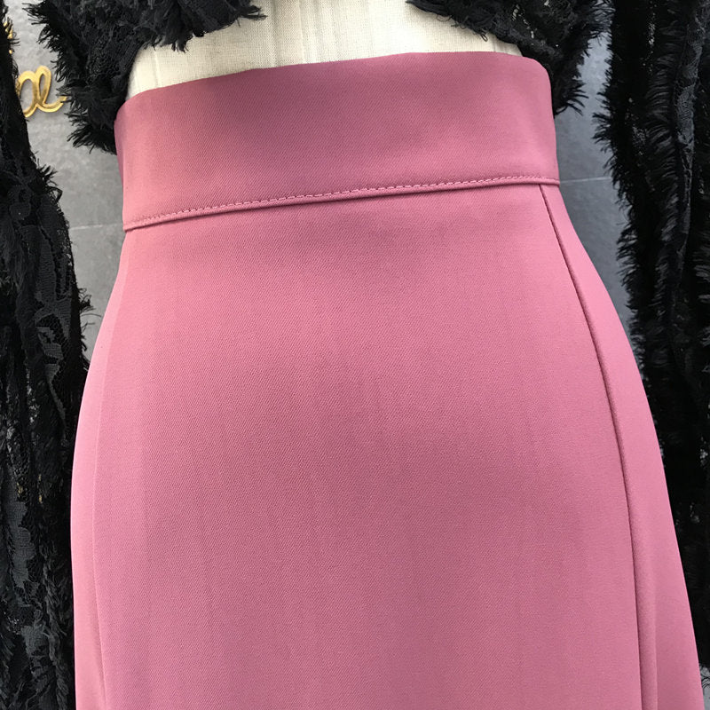 A close-up of a pink high-waisted pencil skirt displayed on a mannequin torso, flanked by black lace and feather-trimmed sleeves.