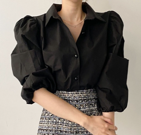 Person wearing a black blouse with puffed sleeves on a plain background