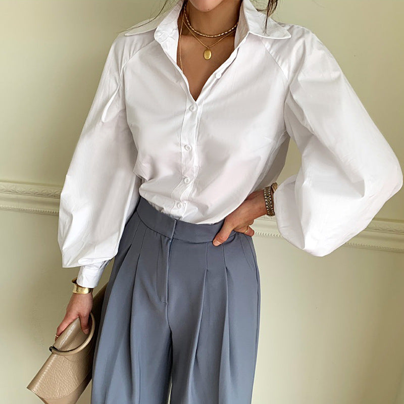 Person wearing a white satin shirt and gray pants against a plain background