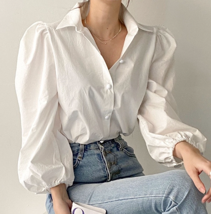 Person wearing a white blouse with puffed sleeves and blue jeans against a neutral background