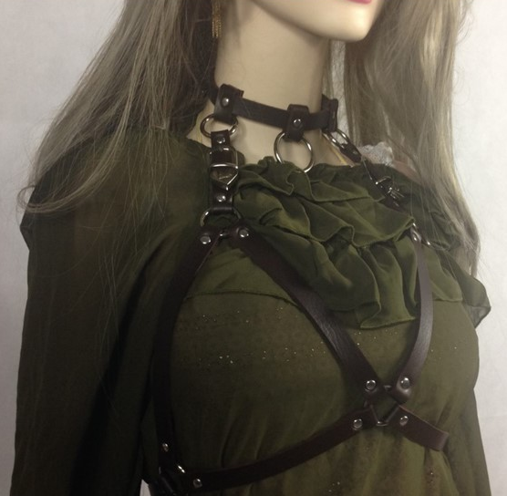 Mannequin wearing a green top with a black harness on a plain background