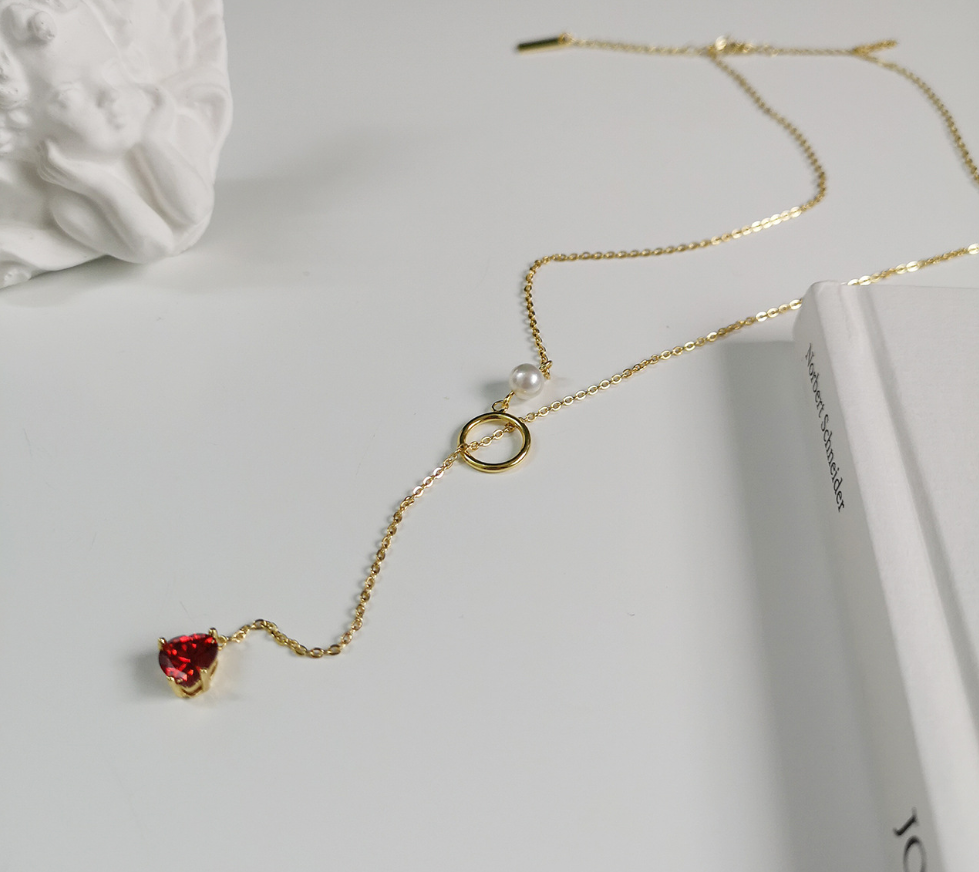 Gold necklace with a red heart pendant on a white surface
