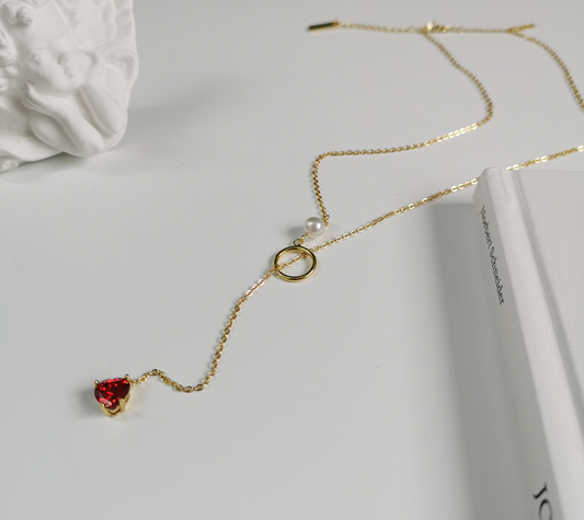 Gold necklace with a red heart pendant on a white surface