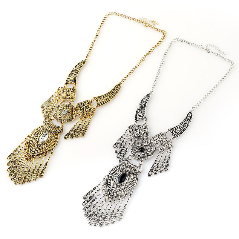 Two ornate statement necklaces with detailed filigree and fringe designs, one in gold-tone metal and one in silver-tone metal, displayed on a clean white background.