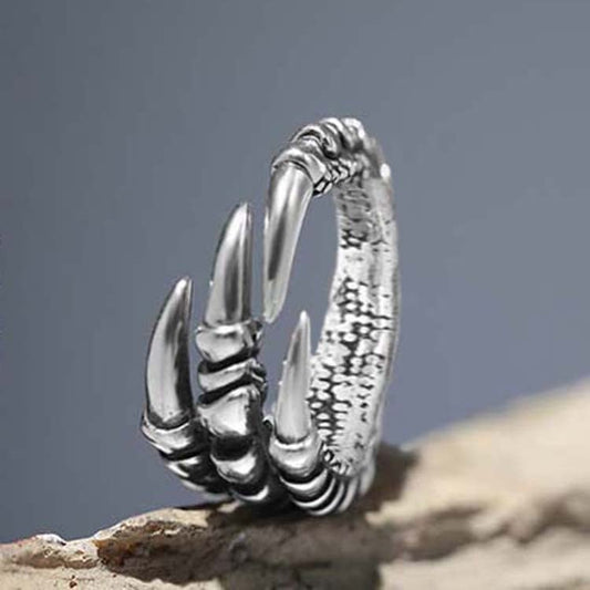 Silver claw-like ring on a textured surface with a gray background