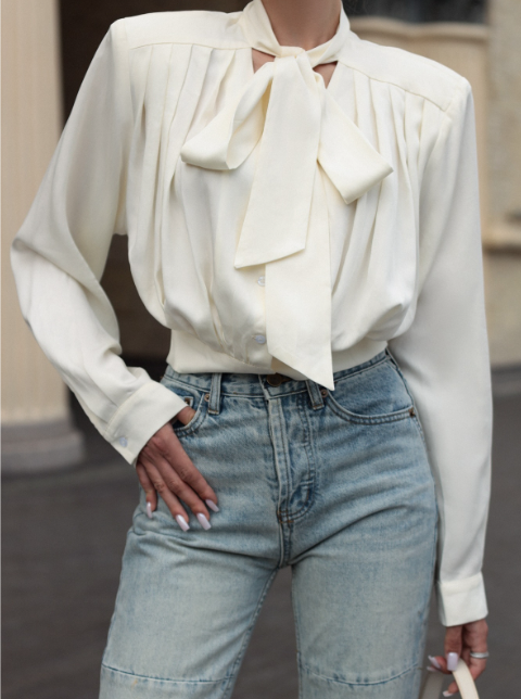 White blouse with a large bow and blue jeans worn by a person.