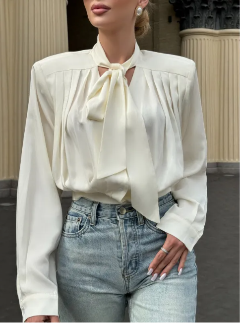 Woman wearing a white blouse with a tie detail and blue jeans in an urban setting.