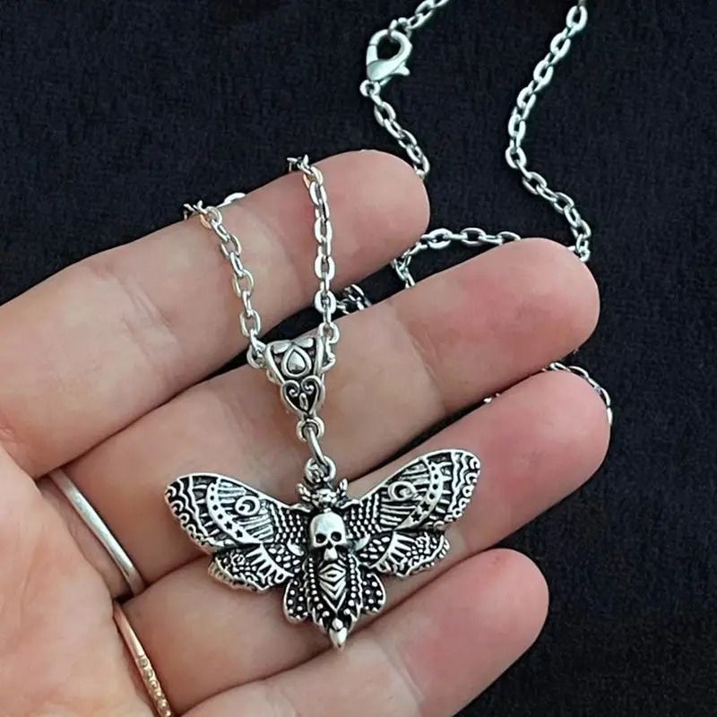 Silver butterfly pendant necklace held in a hand against a black background
