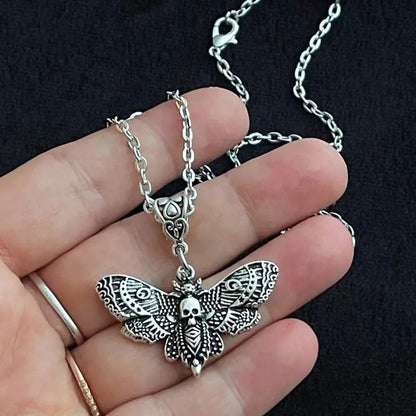 Silver butterfly pendant necklace held in a hand against a black background
