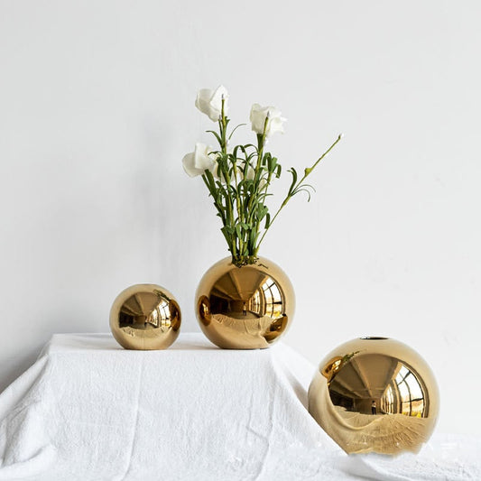 Gold spherical vases with white flowers on a white surface and background