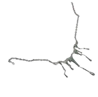 A silver-toned necklace with a dripping, tree-like pendant design, displayed on a white ceramic plate against a white textured fabric background.